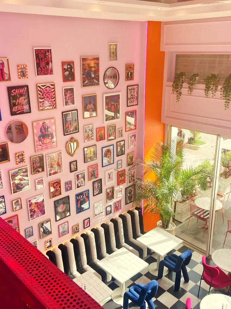 Le mur rose couvert de cadres pop art, vu depuis la mezzanine, au-dessus d'une banquette rayée noir et blanc